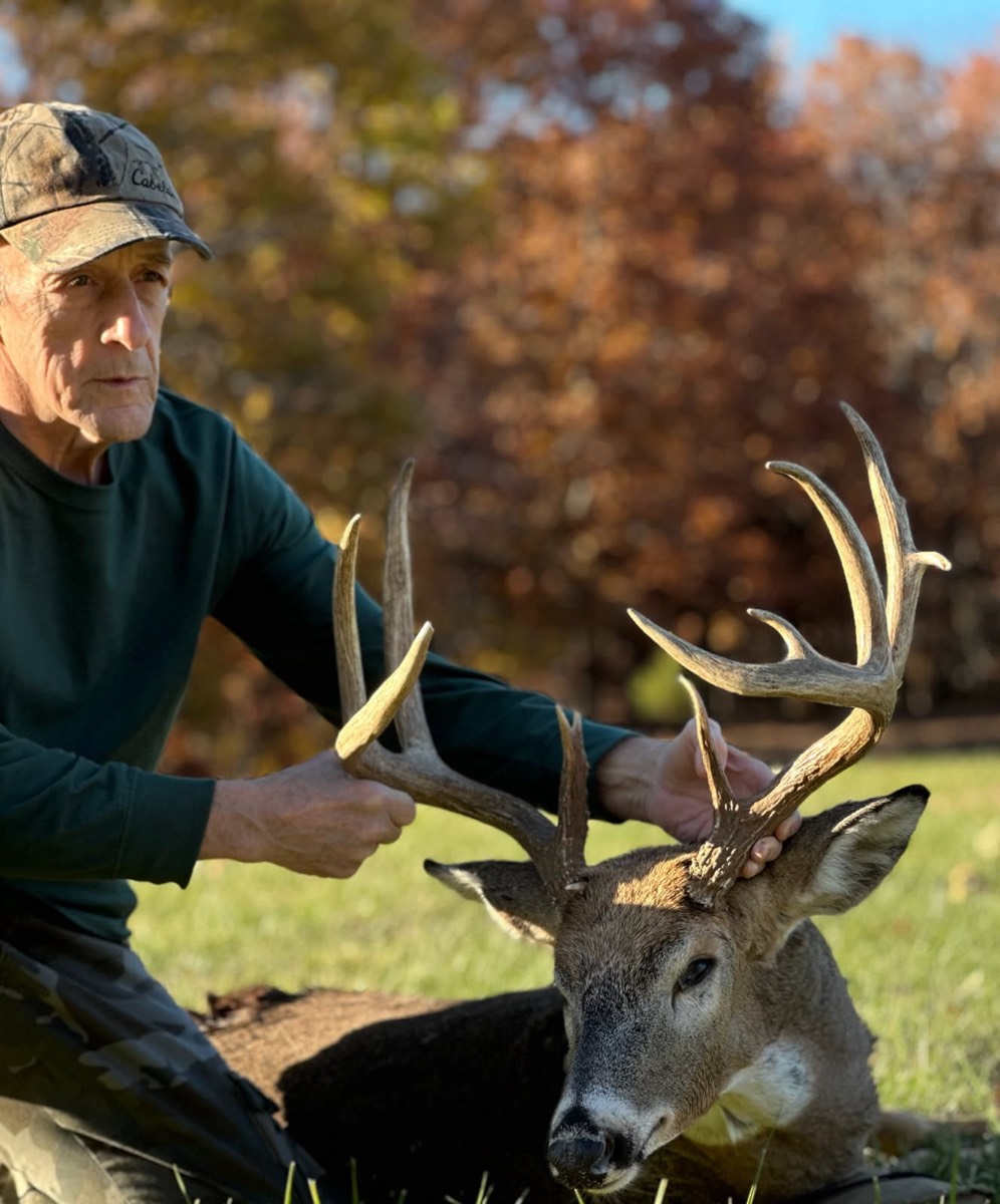 Hunter holding the rack of a tall-tined whitetail buck against fall timber