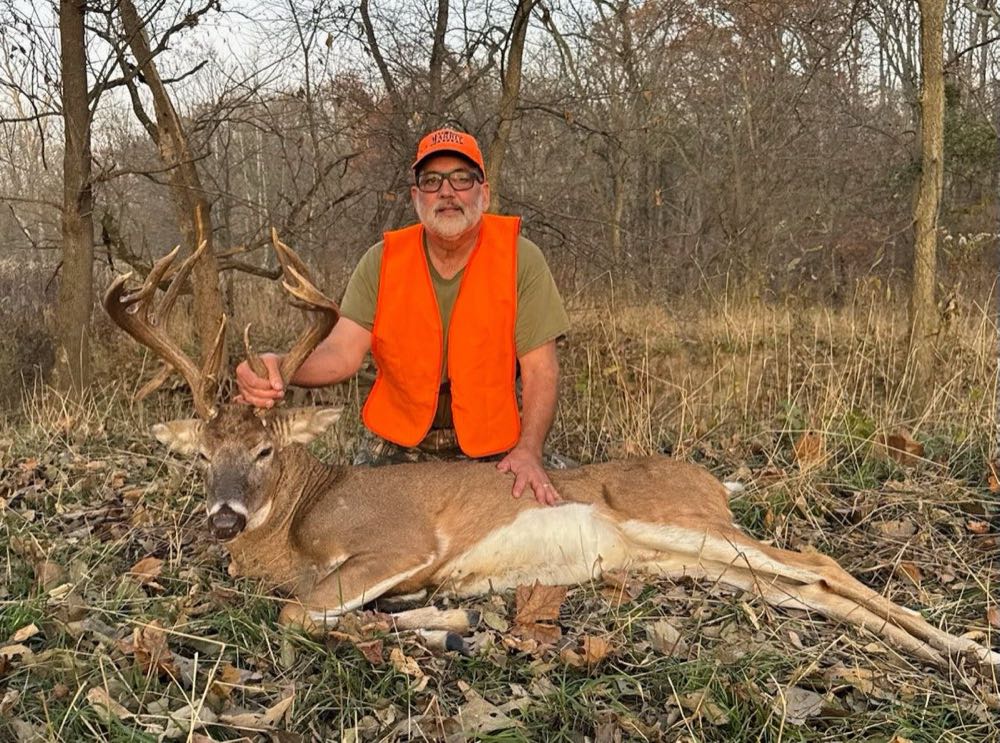Hunter in a blaze-orange vest kneeling behind a harvested Missouri whitetail buck