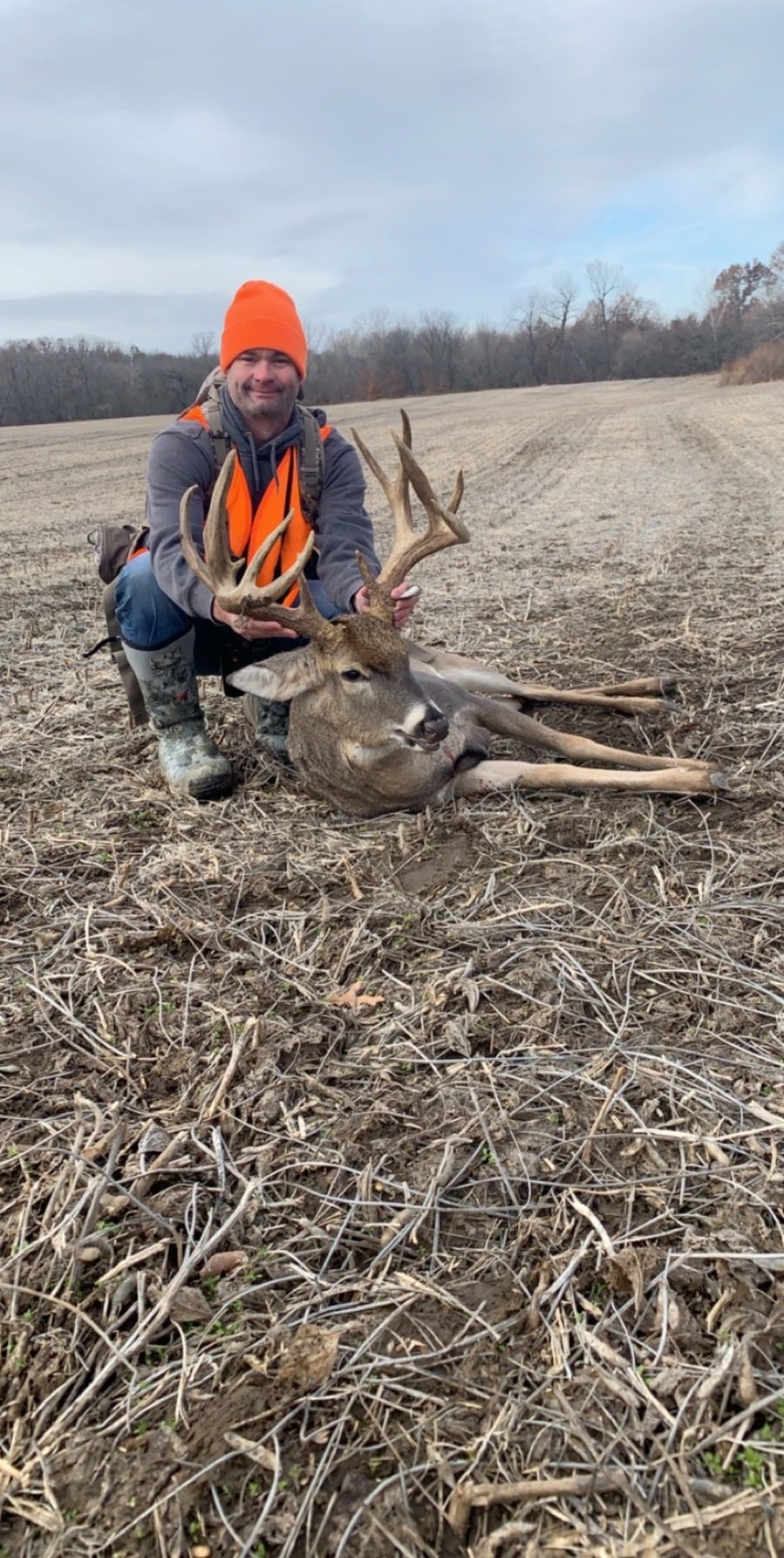 Hunter in blaze orange kneeling with a heavy Missouri whitetail buck in a harvested field