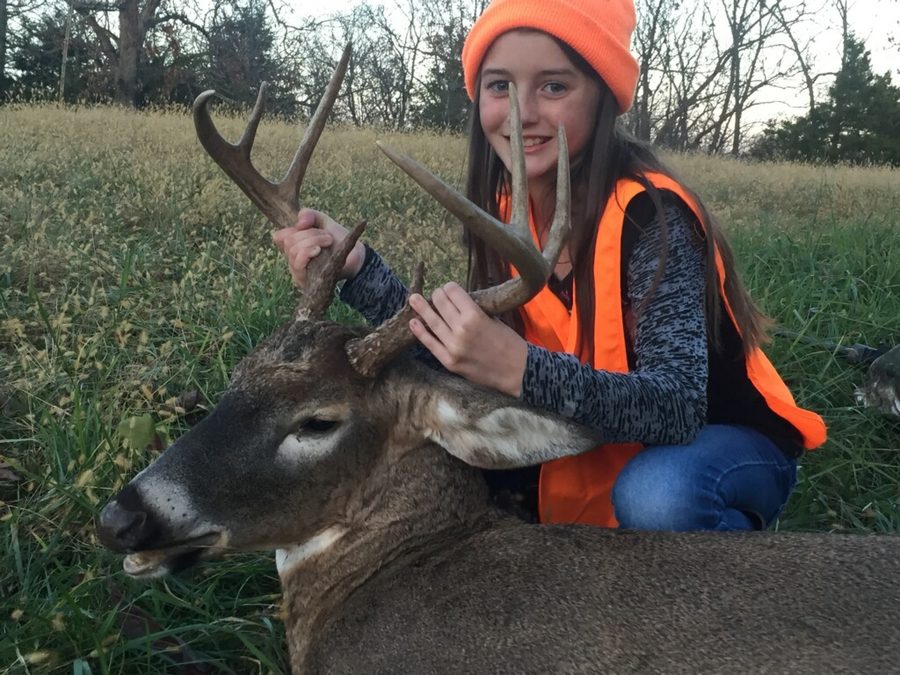 Young hunter with a Missouri whitetail buck in a grass field at dusk