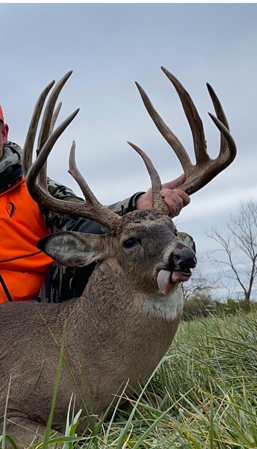 Hunter holding up the rack of a tall-tined Missouri whitetail buck in a grass field
