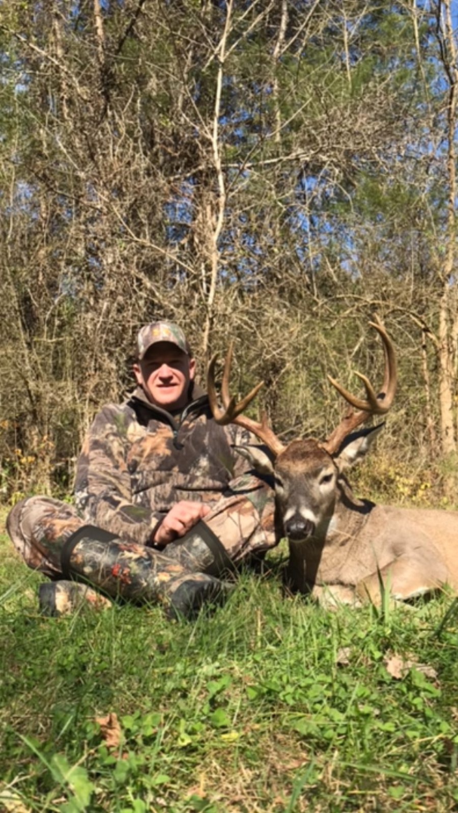 Hunter sitting beside a Missouri whitetail buck in the timber on a sunny afternoon