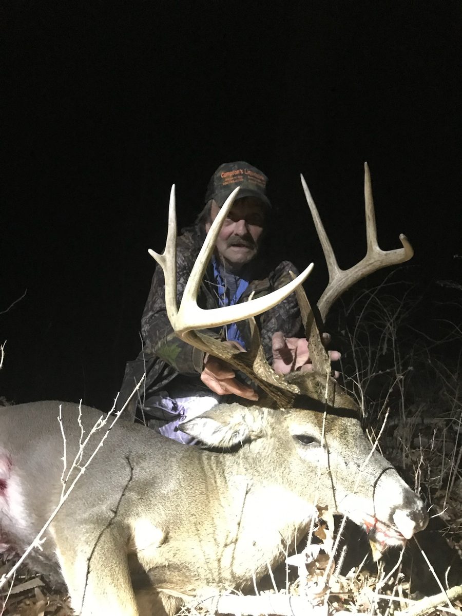 Hunter holding the rack of a heavy whitetail buck at night