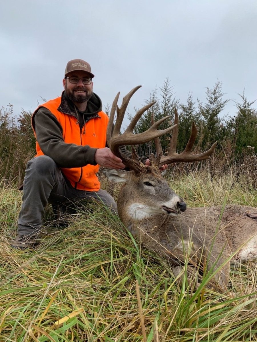 Hunter kneeling behind a long-tined Missouri whitetail buck in an open field